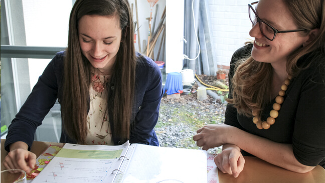 Elise zit achter een cursusmap met haar GON-begeleidster