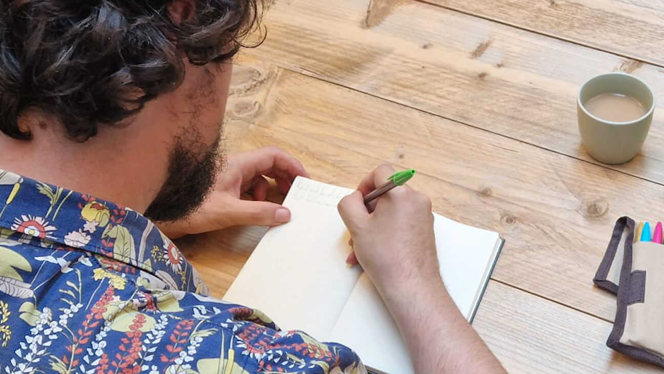 Persoon schrijft in boekje bij een Creatief Schrijven workshop
