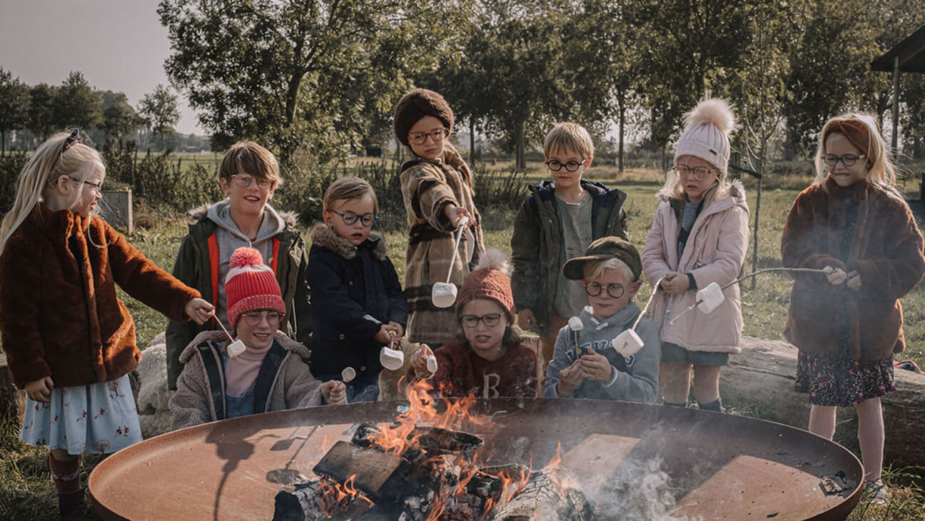 Kinderen met bril zitten rond een kampvuur