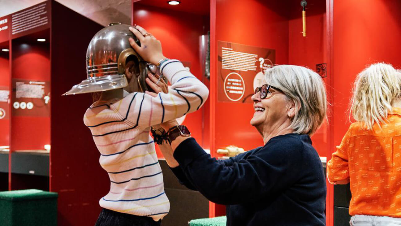 Jongen past Romeinse helm in Regionaal Archeologisch Museum Maaseik