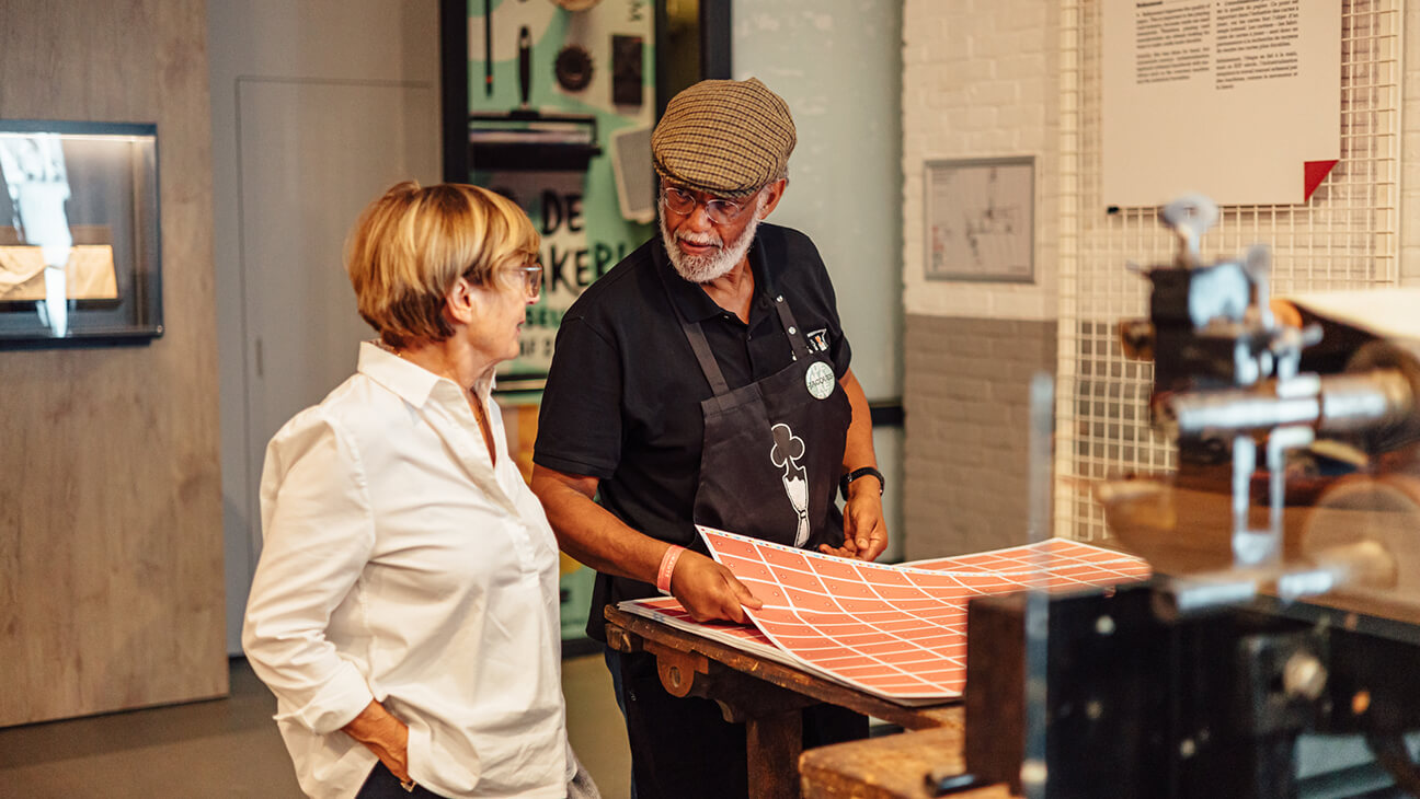 Bezoeker bij een gids aan de historische drukpers in het speelkaartenmuseum