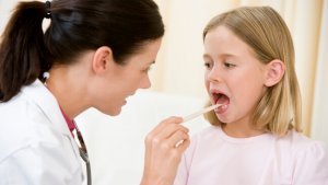 Doctor giving checkup to young girl with tongue depressor in exam room