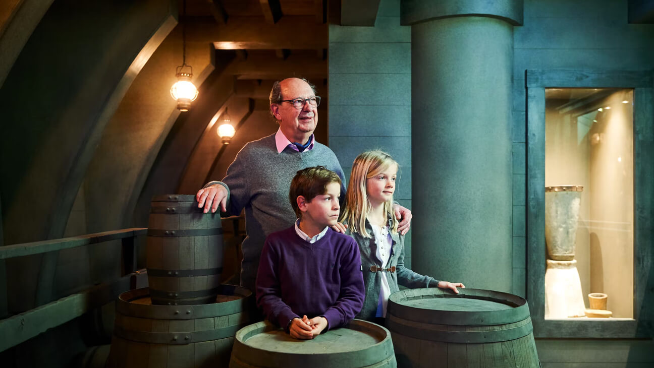 Opa en kleinkinderen bezoeken nagebouwd schip voor de transport van cacao