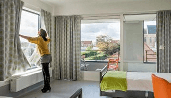 Vrouw opent gordijnen in hotelkamer