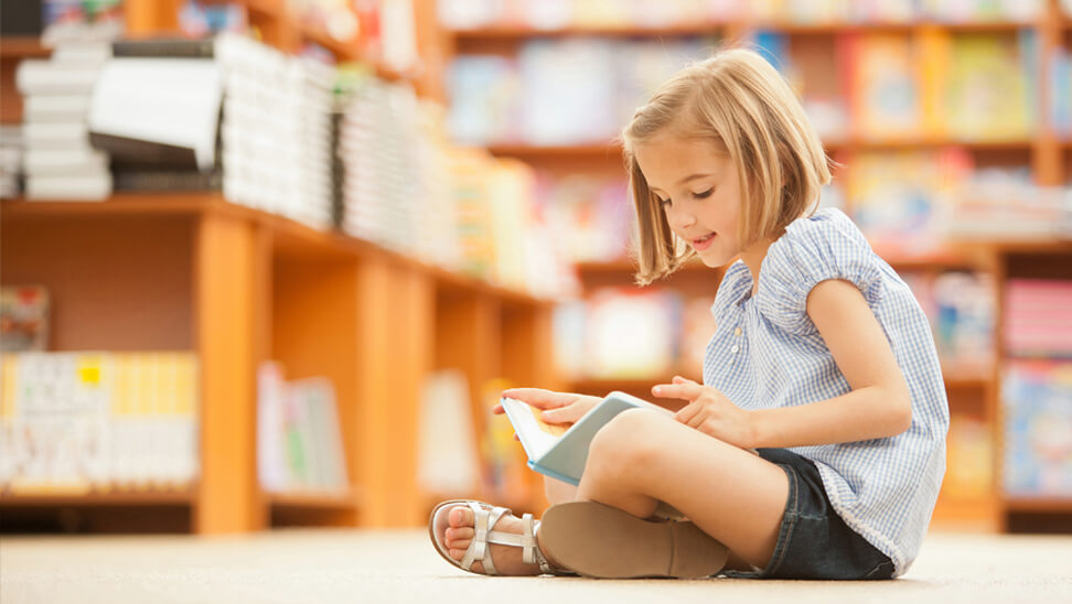 Meisje zit voor boekenrek en leest boek