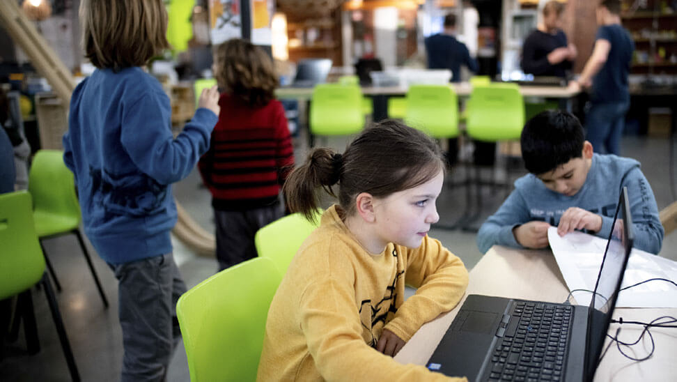 De leerlingen werken in groepjes achter laptops.