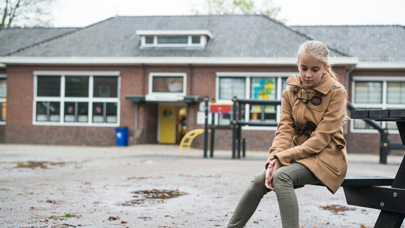 Meisje buiten op een bank aan de school