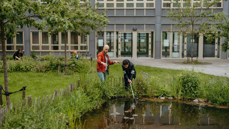 Jonas Jossels begeleidt een leerling die vuilnis uit de schoolvijver schept