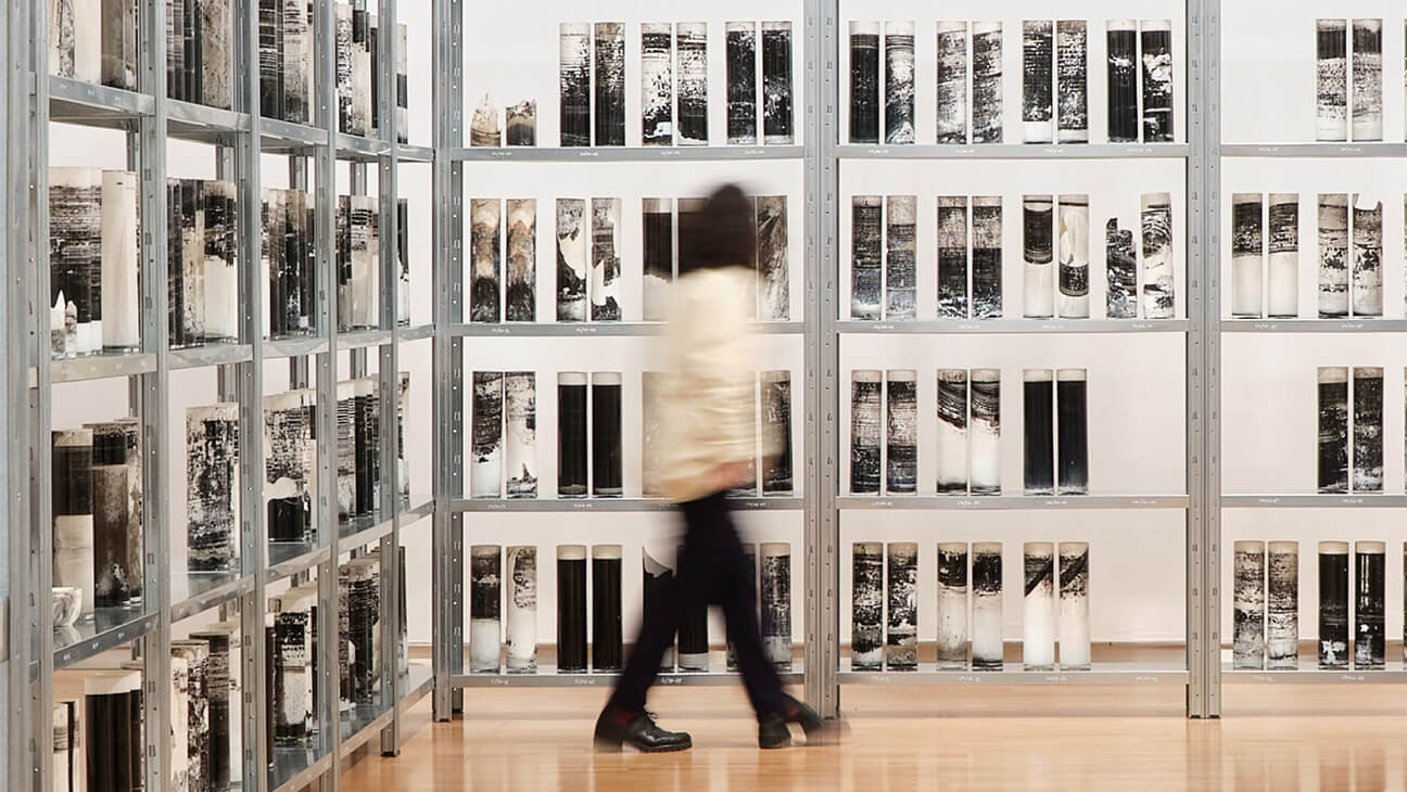 Bezoeker in een zaal met verweerde glazen cilinders op de expo 'Biblioteca Nacional'