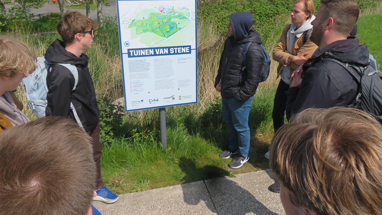 Gids met bezoekers bij een bord over tuinen van Stene